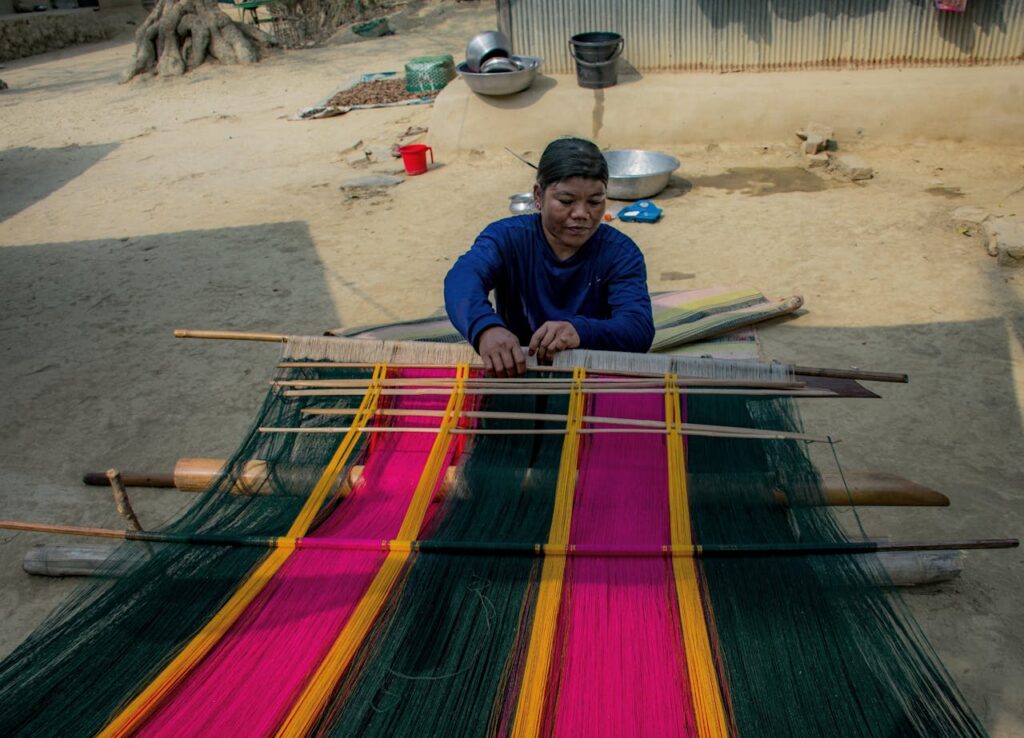 Woman weaving colorful fabric on a handloom in rural Bangladesh.